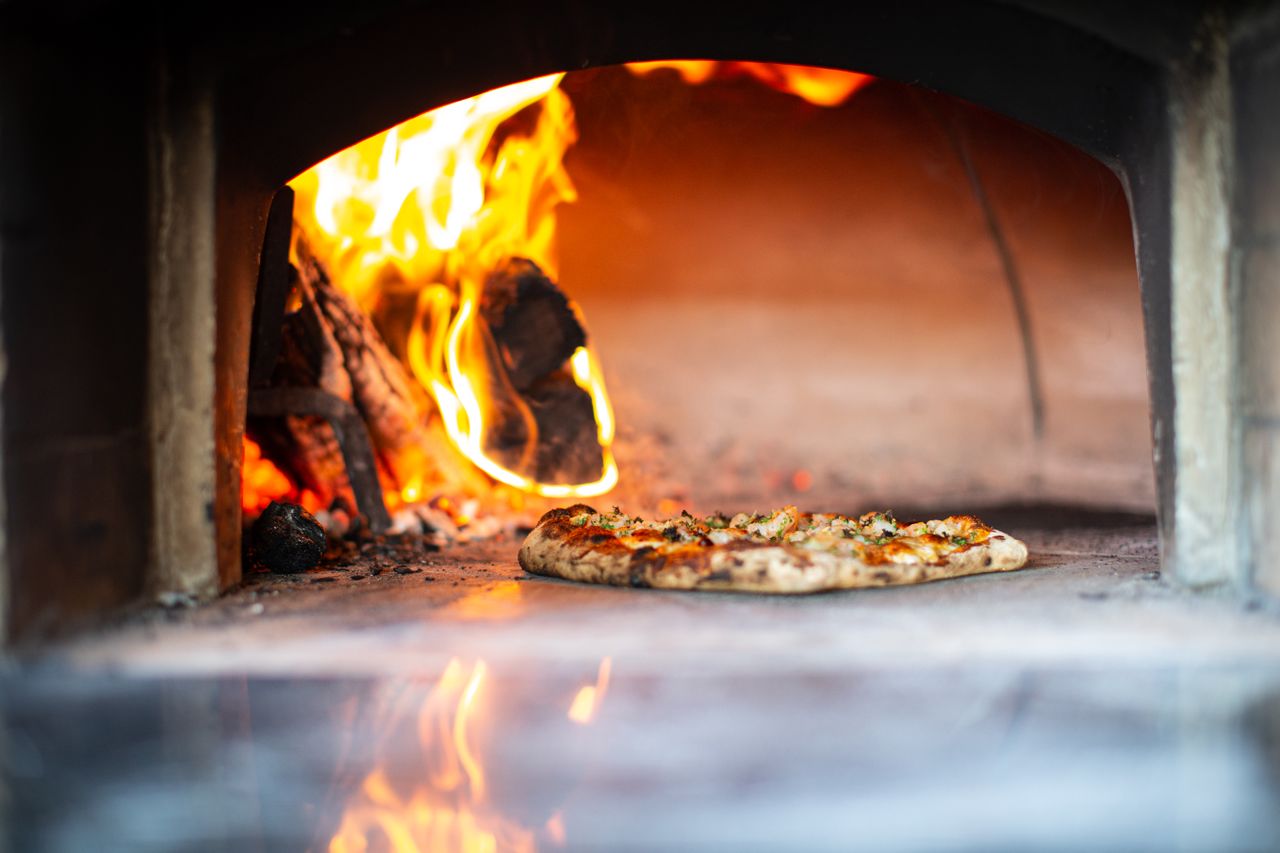 Delicious artisan pizza baking in a traditional wood-fired oven with flames.